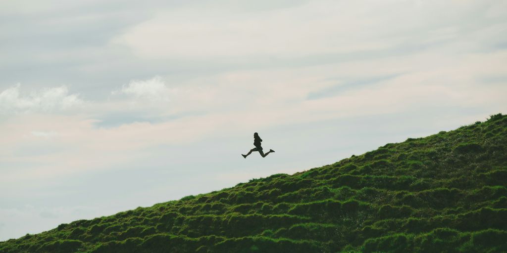 person jumping on grass field under cloudy sky during daytime