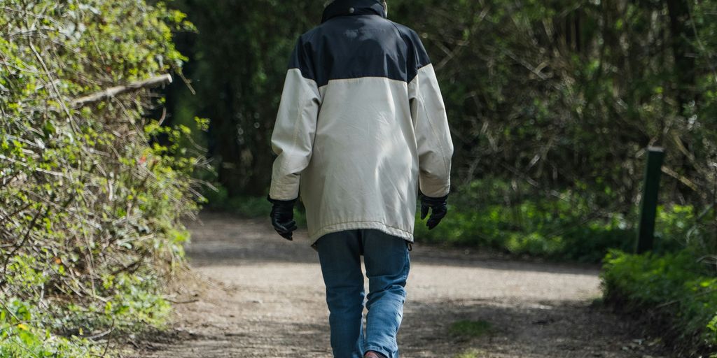 person in white jacket walking on dirt road during daytime