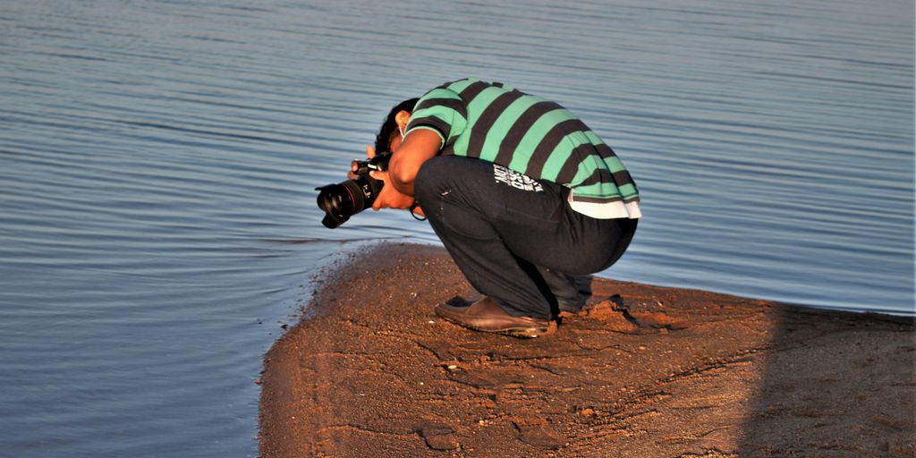 a man kneeling down next to a body of water