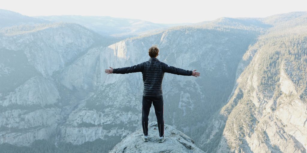 man opening his arms wide open on snow covered cliff with view of mountains during daytime