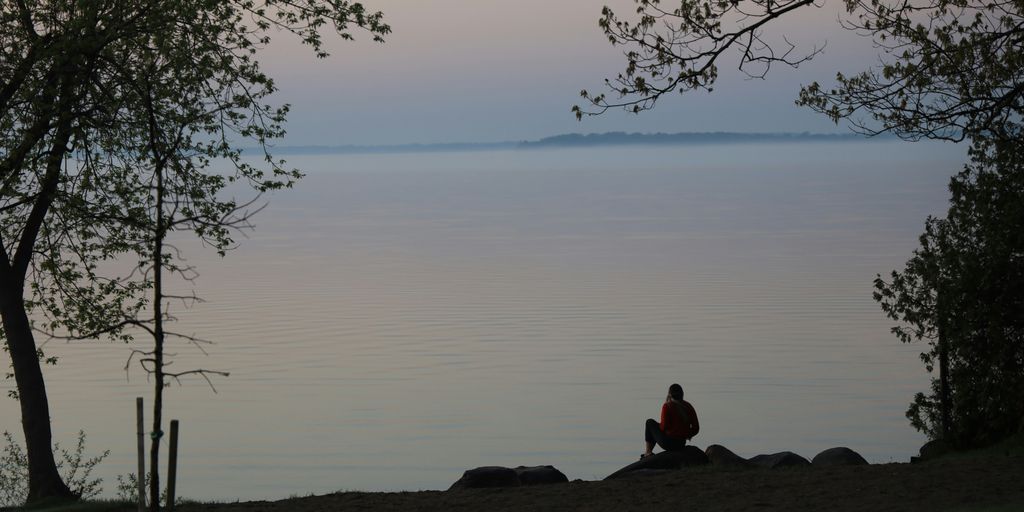 man sitting on rock near body of water during daytime