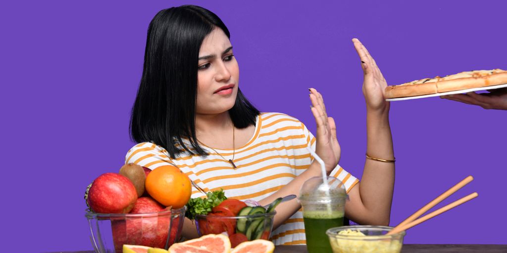 a woman sitting at a table with food and a bowl of fruit