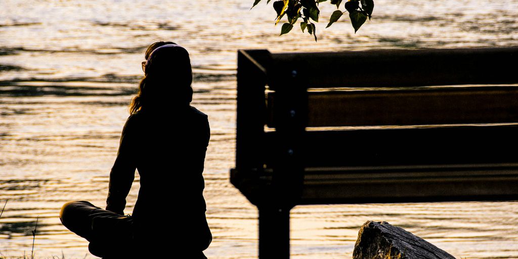 silhouette of person sitting on bench near body of water during daytime