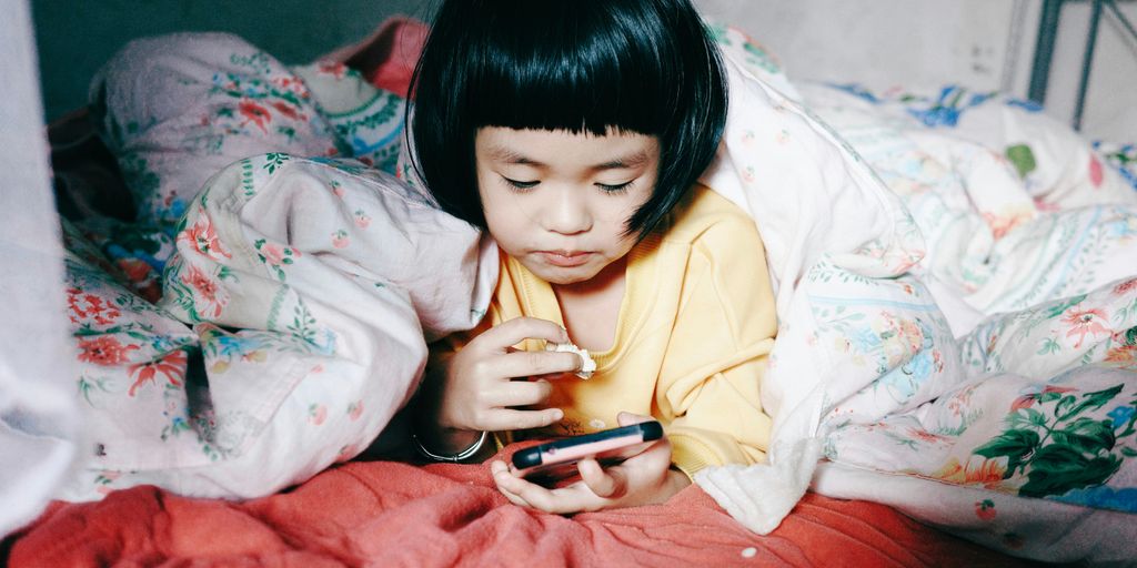 a little girl laying in bed looking at a cell phone