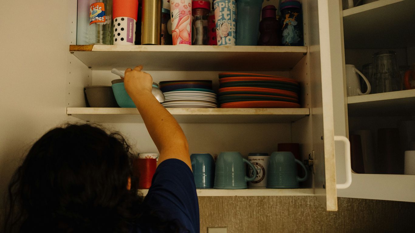 A woman reaching up into a kitchen cabinet