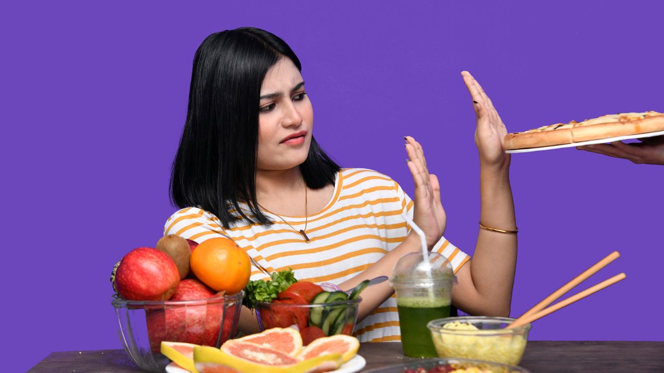 a woman sitting at a table with food and a bowl of fruit