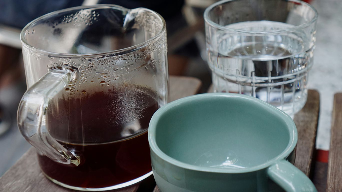 a glass of liquid and a cup of coffee on a table