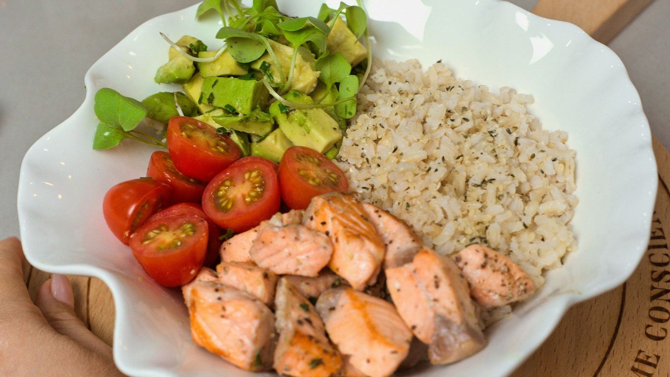 a white bowl filled with chicken, rice, tomatoes and avocado