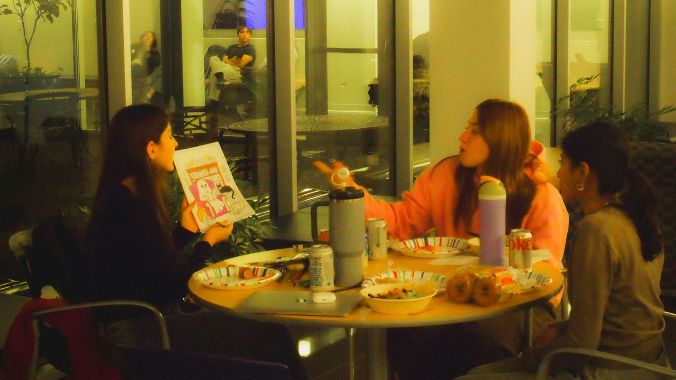 Three women talking at a table with snacks.